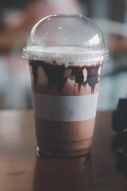 Buzlu kahve, tek kullanımlık plastik bardakta, ahşap masada.