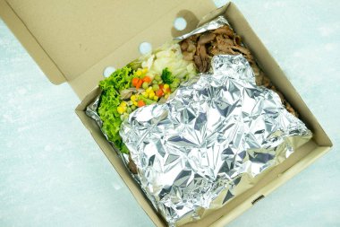 Sebzeli Kore usulü ızgara domuz eti. Kutunun üzerinde folyo kağıdı var..