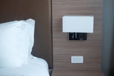 Komodinin ve lambanın ayrıntıları. Yatağın başındaki beyaz yastık ve komodinin üstündeki lamba..