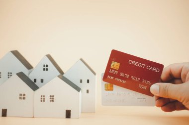 Beyaz model ahşap evde iki kredi kartı tutan adamın eli. Konut işi kavramı