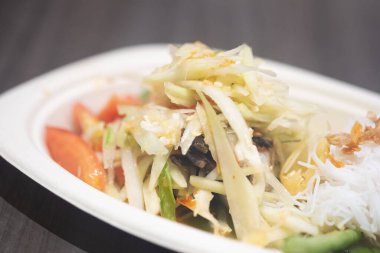 Beyaz kağıt tabakta servis edilen yengeçli Papaya salatası.