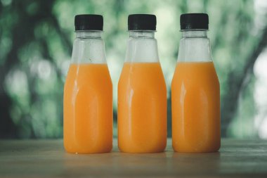 Buz gibi soğuk portakal suyu. Ahşap masada siyah kapaklı üç şişe.