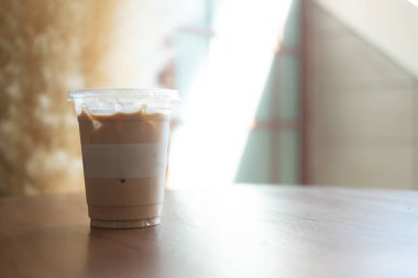 Tahta masanın üzerinde plastik camda buzlu latte. Sabah ışığı, 16ons plastik cam.