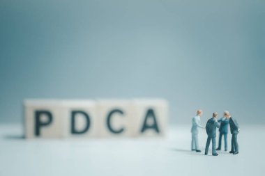 PDCA 'nın bulanık önünde toplanan ve ayakta duran bir grup işadamı (Plan, Do, Check, Action) - dört adım yönetim yöntemi