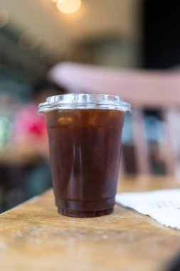 Close up of take away plastic cup of iced black coffee at coffee shop.