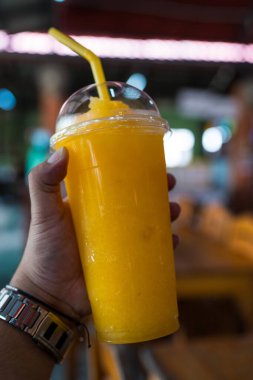 Lezzetli portakallı smoothie, insan eli üzerinde plastik cam.