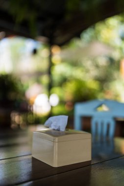 Restorandaki ahşap masanın üzerinde beyaz kare doku kabı var. Arka planda bulanıklık var.