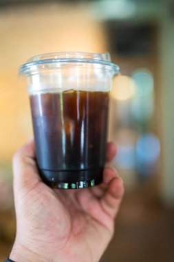 Buzlu Americano tek kullanımlık bardakta, insan elinin üzerinde. Kapat.