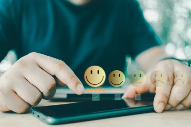 Müşteri memnuniyeti, çevrimiçi geri bildirim derecesi ve müşteri deneyimi konsepti. Akıllı telefonla en iyi hizmeti verdiği için 5 yıldızlı mutlu yüzü seçmek için sanal kontrol işaretine kullanıcı dokunuşu.