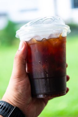 Plastik bardakta soğuk Americano kahvesi insan eliyle arka planda.