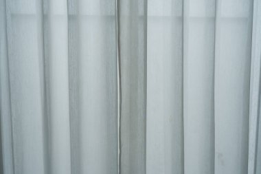 Saf beyaz perdeleri ve daha ağır, koyu bir perdesi olan bir pencere kısmen çekilmiş, yumuşak ışığın içinden geçmesine olanak sağlıyor..