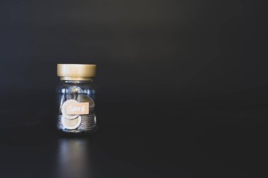 Siyah arkaplana para dolu tasarruf kavanozu, gelecek için mali planlamayı ve para yönetimini sembolize ediyor.