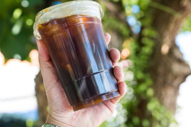 Tarafsız arka plana karşı çevreye dost olmak için pipet kullanmaya gerek olmayan bir bardak soğuk nitro koyu kahve tutan el.