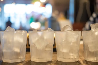 Ahşap masanın üzerinde buz küpleri olan bir sıra cam.