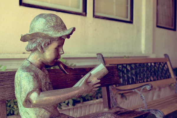 Escultura de menino lendo um livro no banco com filtro vintage desfoque fundo — Fotografia de Stock