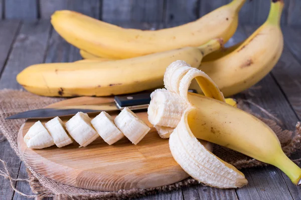 Plátanos y rodajas de plátano en una tabla de madera — Foto de Stock