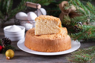 Noel ağacı dalları, koniler ve oyuncaklarla ahşap bir masada beyaz bir tabakta ev yapımı pandispanya. Yeni yıl ve Noel tatlısı. Pasta..