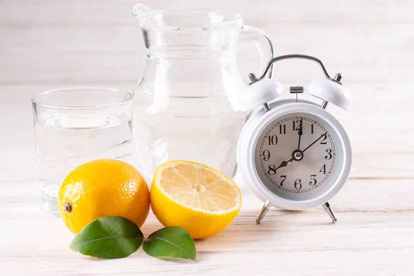 Alarm clock and a detox glass of water with lemon on table.