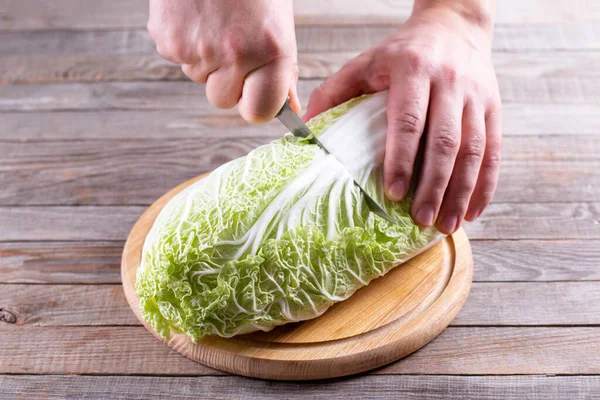 Chinese cabbage on chopping board being cut by kitchen knife in hand on a wooden table