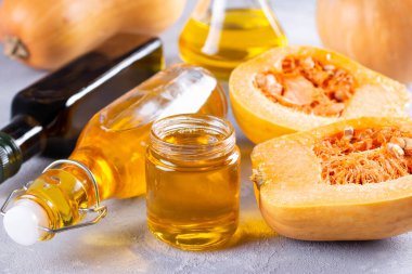 Cam kavanozda balkabağı tohumu yağı ve gri arka planda taze çiğ pampkin. Sağlıklı beslenme, diyet veya vegan gıda konsepti.