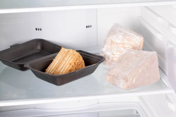 Honey cake Medovik packed in cling film in a refrigerator. Frozen cake