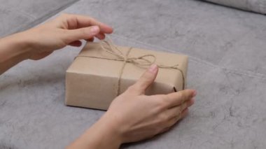 Hands of woman unwraps the gift, removing jute rope from gift box. Gifts Packed with your own hands. Zero waste gift wrapping