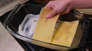 A woman in the kitchen prepares lasagna: pasta of lasagna, adds cheese, red minced meat sauce (bolognese) and white sauce (bechamel). Cooking lasagna