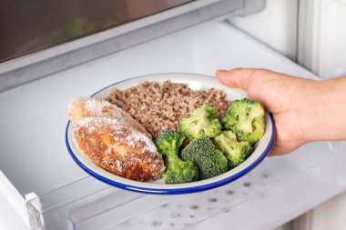 Eller buzdolabından bir tabak donmuş pirzola ve sebze alıyor. Hazır yiyecek depolama kavramı
