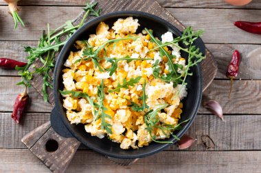 Tahta bir masa üzerinde mısır, peynir ve roka ile çırpılmış yumurta, üst manzara. Nefis ev yapımı kahvaltı.