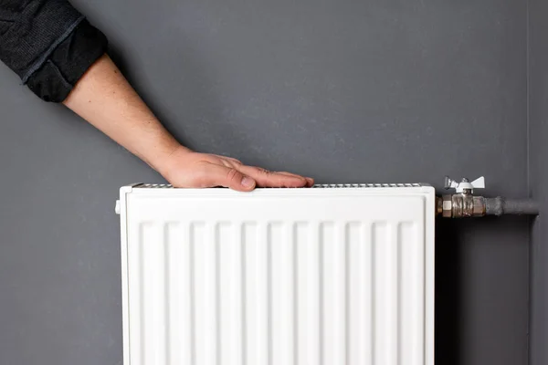 Man warming hands on heating radiator near gray wall, closeup