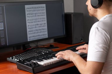 Evde bilgisayarla çevrimiçi piyano çalmayı öğrenen bir adam. Kendi kendine öğrenme kavramları, evde kalmak ve online çalışmak.