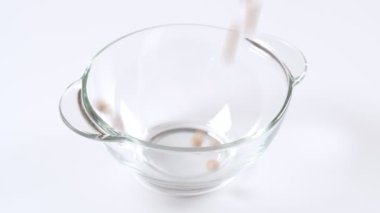 Kuru, çiğ bezelyeler beyaz arka planda cam bir kaseye düşüyor, ağır çekim.