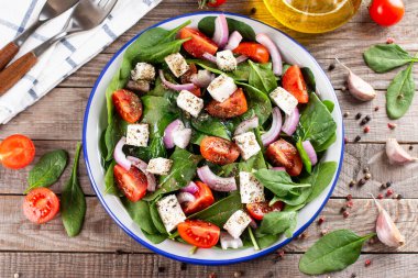 Ispanak, domates, peynire ait taze sebze salatası, ahşap bir masada tabakta soğan. Üst görünüm