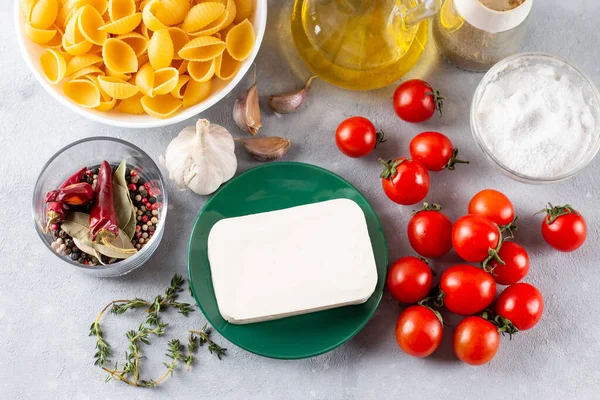 Preparation of ingredients for feta pasta. Trending Feta bake pasta recipe made of cherry tomatoes, feta cheese, garlic and herbs on a light background. Top view, above, copy space.