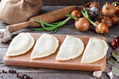 Ahşap arka planda çiğ cheburekler. Çiğ hamur ve kıyma ile ev yapımı kavramı, yatay.