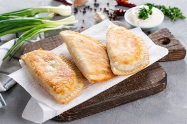 Etle süslenmiş, gri arka planda yeşilliklerle süslenmiş Cheburek. Geleneksel Kafkas mutfağı, yakın plan.