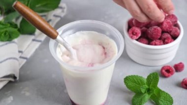 Ahududu, plastik kavanozda beyaz Yunan yoğurdunun içine düşer. Organik böğürtlen, temiz yemek, vegan gıda konsepti. Taze sağlıklı yiyecekler..