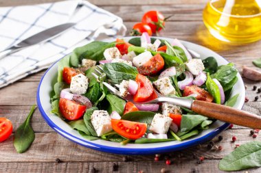 Ispanaktan taze sebze salatası, domates, feta peyniri, ahşap bir masada tabakta soğan.