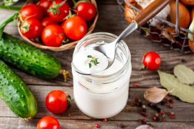 Sour cream in a jar with vegetables on the background. Dressing for salads and vegetables