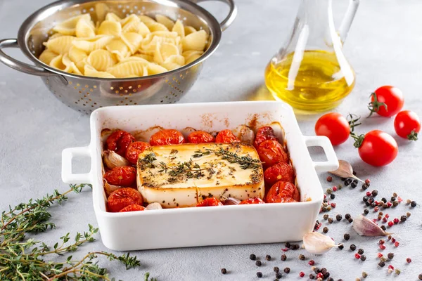 Feta cheese pasta sauce recipe step. Small tomatoes drizzled with olive oil in a baking dish with a feta cheese block in the middle and sprinkled with salt and freshly ground pepper.