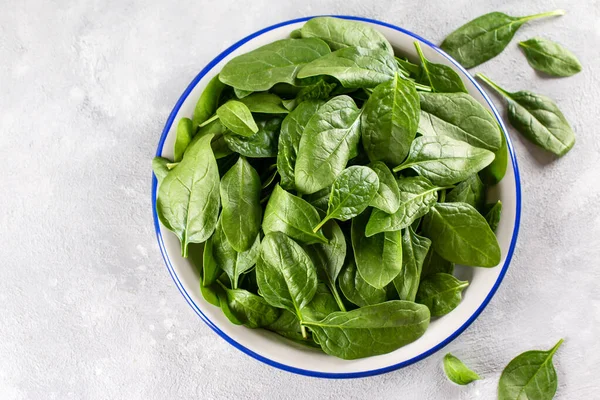 Fresh Spinach Leaves. Raw Spinach in a bowl for vegetarian or vegan salad or smoothie on a gray concrete background. Top view, copy space.