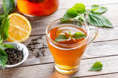 Isırgan otuyla çayı iyileştiriyorum. Ahşap bir masada cam bardakta çay. Halka açık tedavi. Vitaminlerin kaynağı.