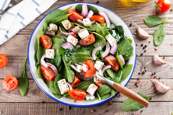 stock image Fresh vegetables salad from spinach, tomato, feta cheese, onion in plate on a rustic wooden table. Top view