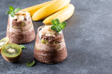 Kakao chia tohumu pudingi, kivi ve muzlu koyu gri masada. Fotokopi alanı ile sağlıklı vegan kahvaltı.