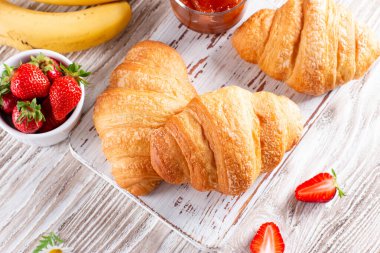 Fresh croissants with jam for breakfast on wooden table. French pastry. Top view