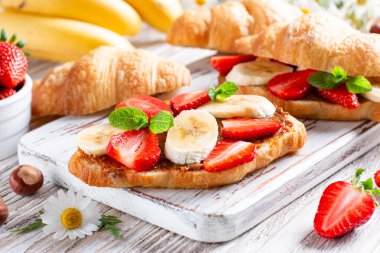 Delicious breakfast with fresh croissants, banana and strawberry on wooden table. French pastry