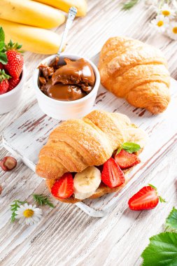 Croissant with chocolate butter, banana and strawberry on wooden table. French pastry