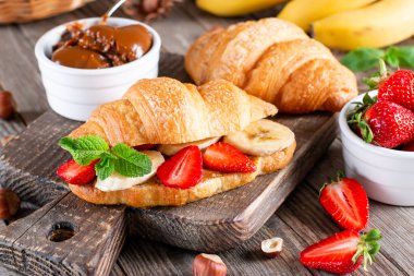 Delicious breakfast with fresh croissants, banana and strawberry on wooden table. French pastry