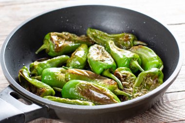 Ahşap bir masada tavada tuzlu ve zeytinyağlı hakiki İspanyol Padron biberleri.