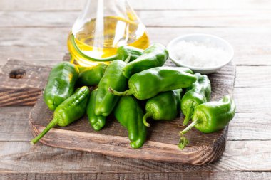 Taze yeşil biberler ya da asma biberler, deniz tuzu, ahşap bir masada zeytinyağı. İspanyol mutfağı. Seçici odaklanma. Pimientos de Padron.
